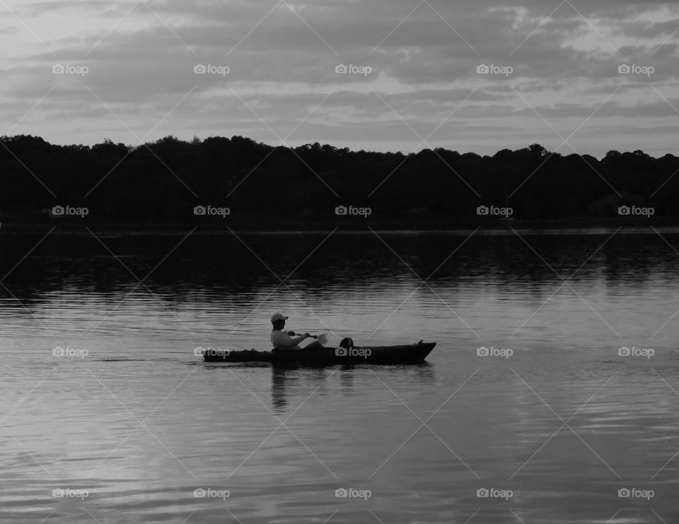 Man and dog in a Kayak. Paddling along on the Choctawhatchee Bay with his companion, dog while enjoying the fresh air and the magnificent sunset