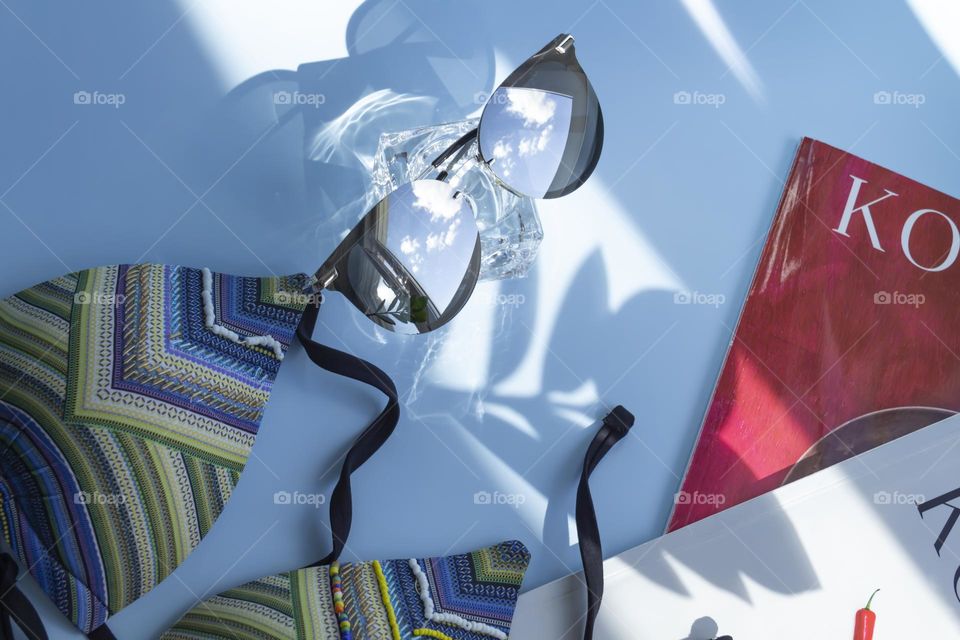 Items prepared for travel.  Swimsuit , magazines sunglasses on a blue background.