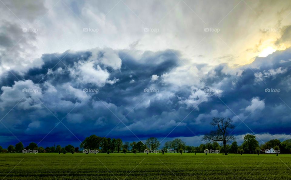 Sun breaking through behind and above the dramatic and dark clouds over a green Grassy Countryside landscape