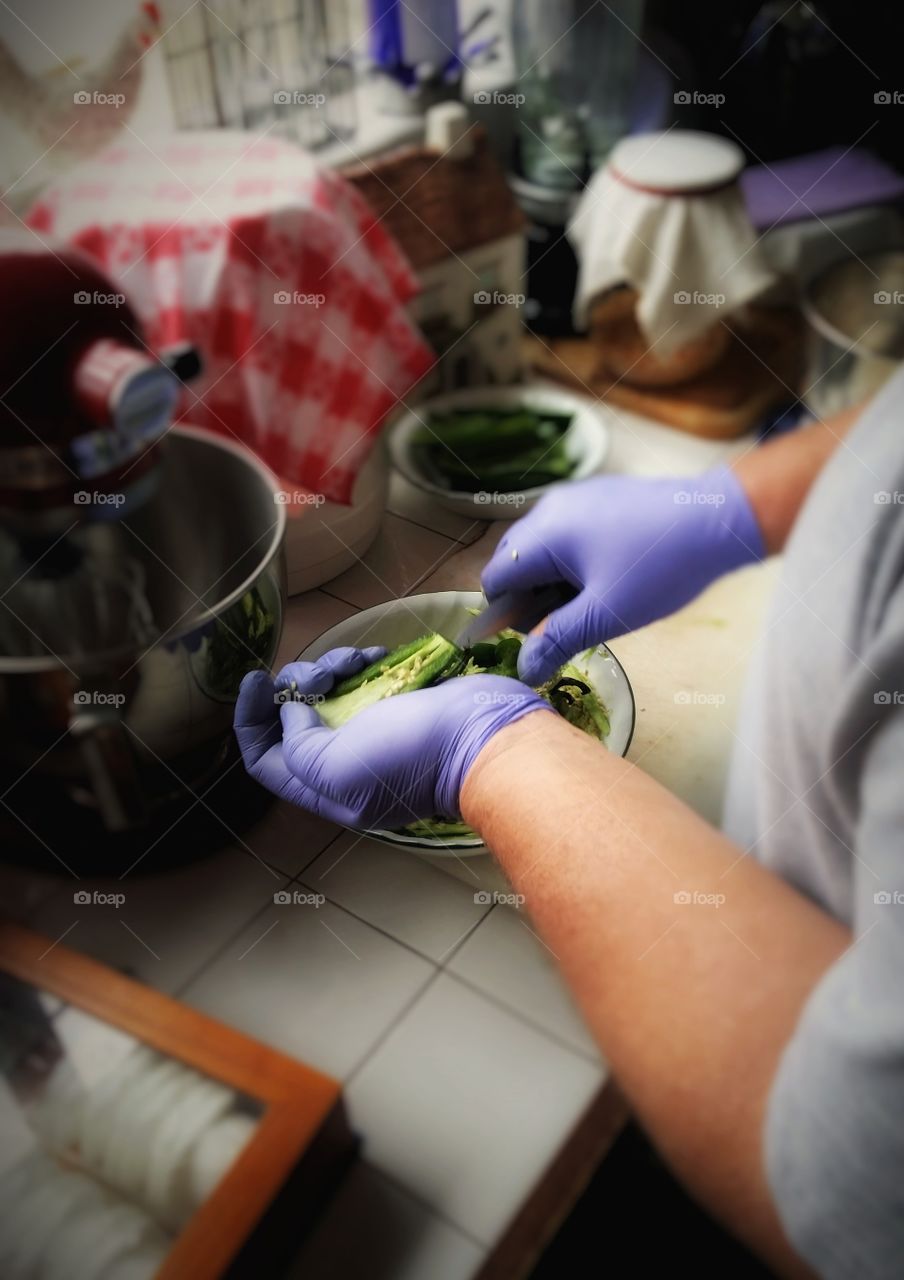 A man wearing purple gloves prepping jalapeño peppers by removing the seeds to stuff them, cooking hobby