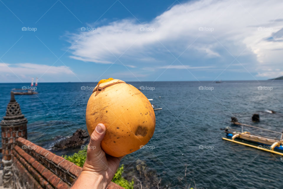 A man holds a coconut in his hand against the backdrop of the Indian Ocean. Bali island.