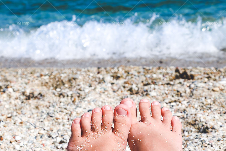 Abstract image of 2020 summer. Selective focus of child's feet on blurred sea background.