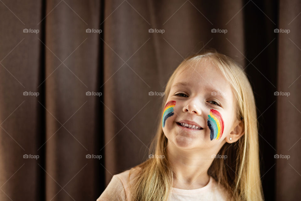 Happy little Caucasian girl with blonde hair and painted rainbow on face