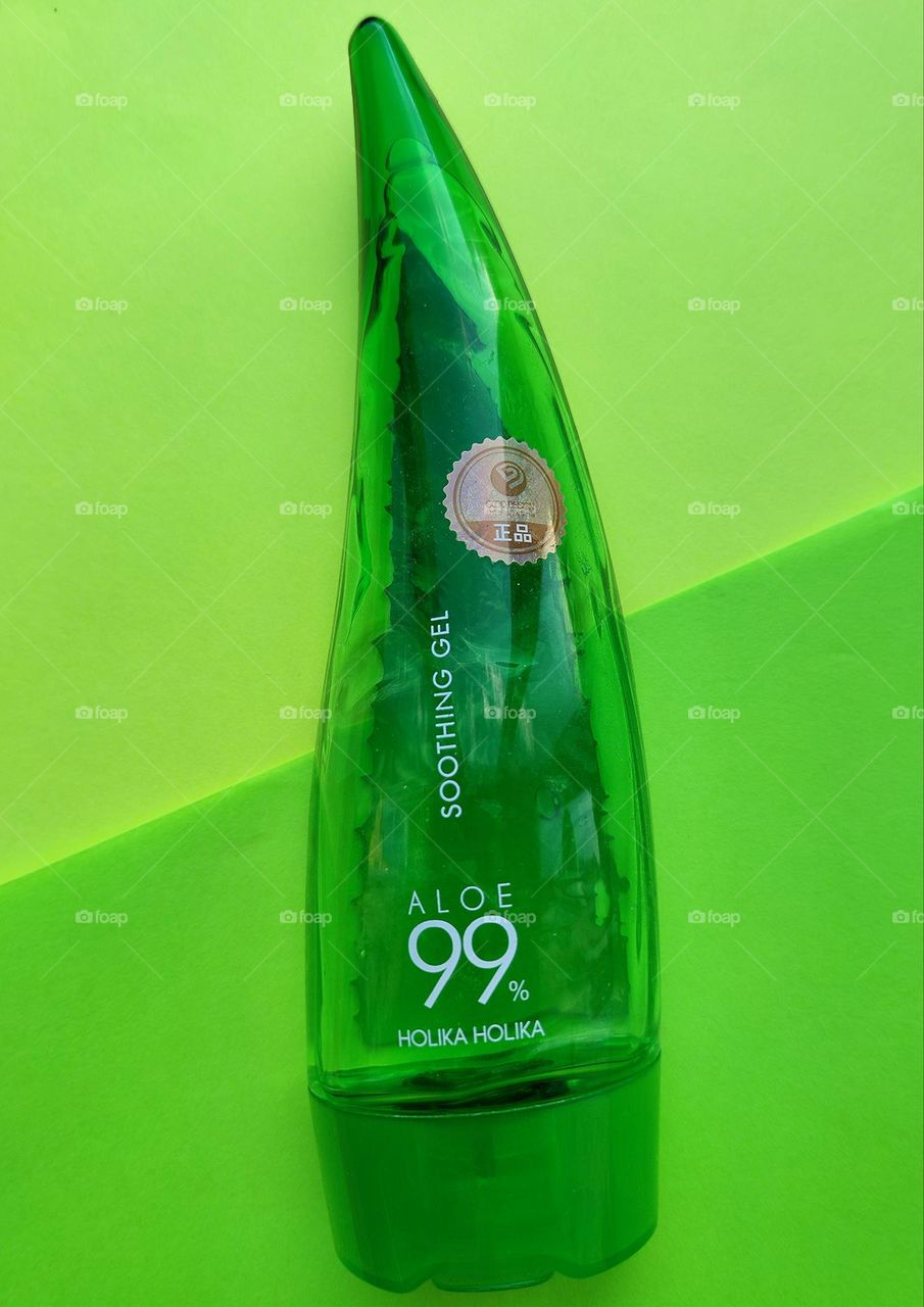 Holika Holika Aloe 99% Soothing Gel. The contrast of the background of dark green and light green, on which lies a green tube of aloe vera gel for face and body