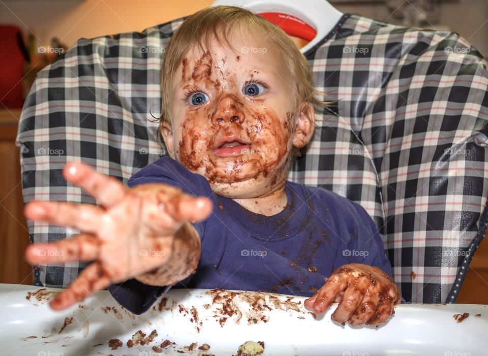 Baby with messy food-covered face reaches for camera taking his picture 