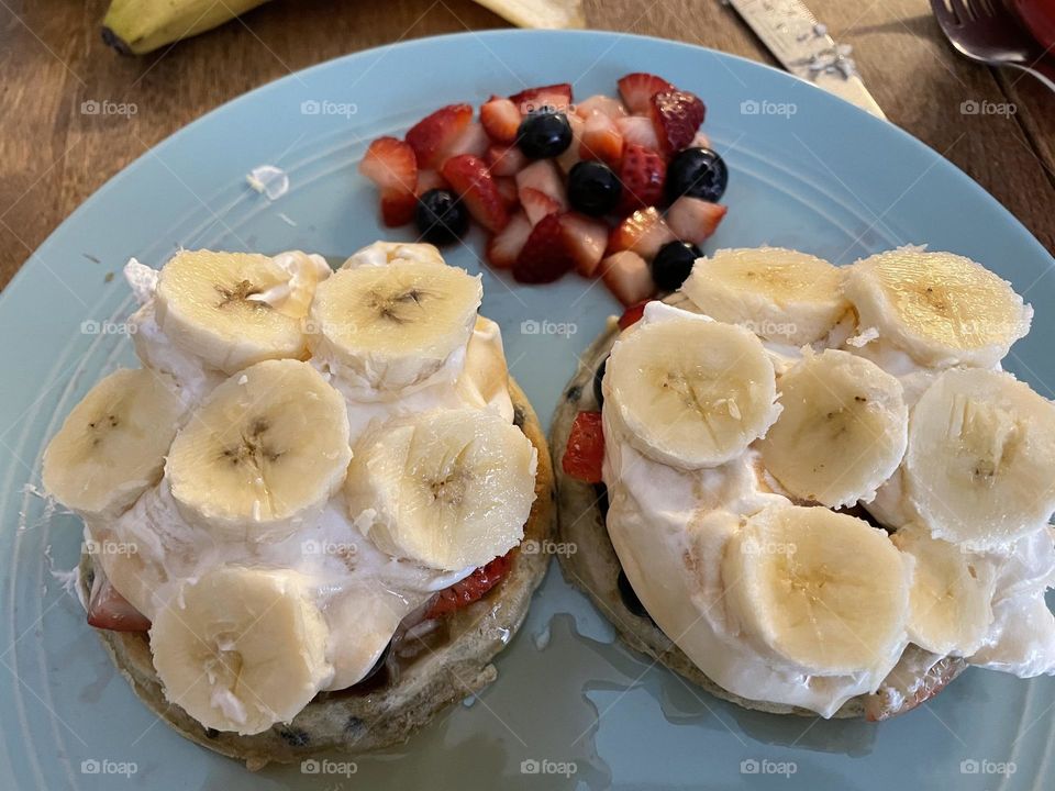 Homemade Mixed fruit salad, with blueberries and strawberries,on the side of these blueberry waffles, with some fruit salad on top, whipped cream and bananas, drizzled with butter maple syrup, on a teal coloured plate, so nummy and filling