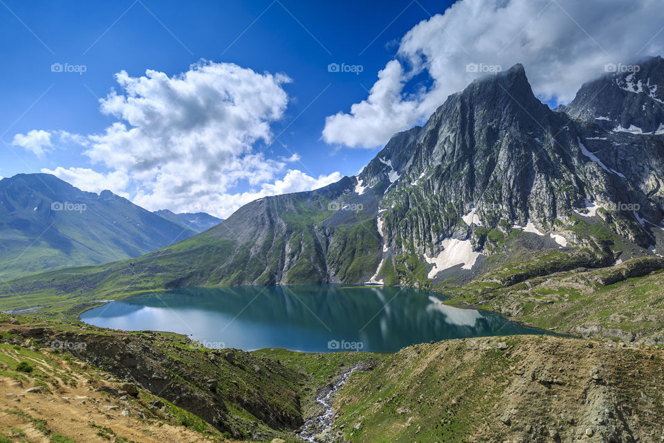 blue sky with white puffy clouds behind mighty mountain and tranquility of the lake. nature at its best
