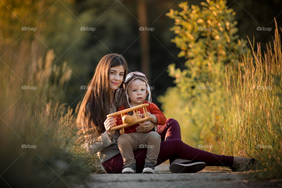 Mother with son playing with wooden plane at sunset