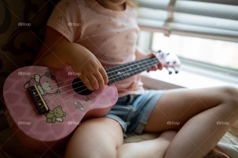 Little Caucasian girl playing on ukulele at home