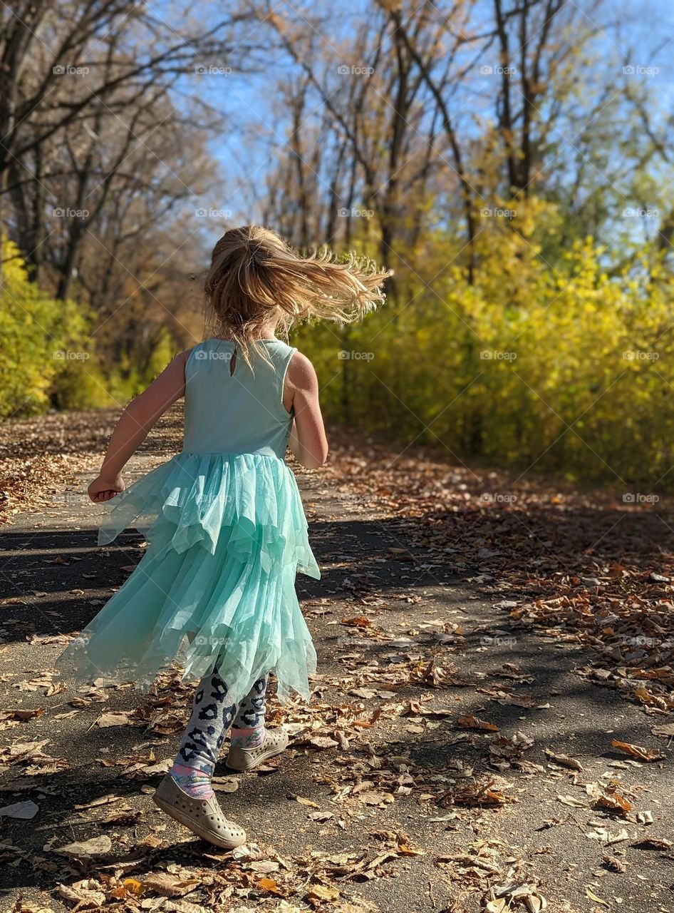 girl running in nature in a teal fancy dress with the fall colors surrounding her