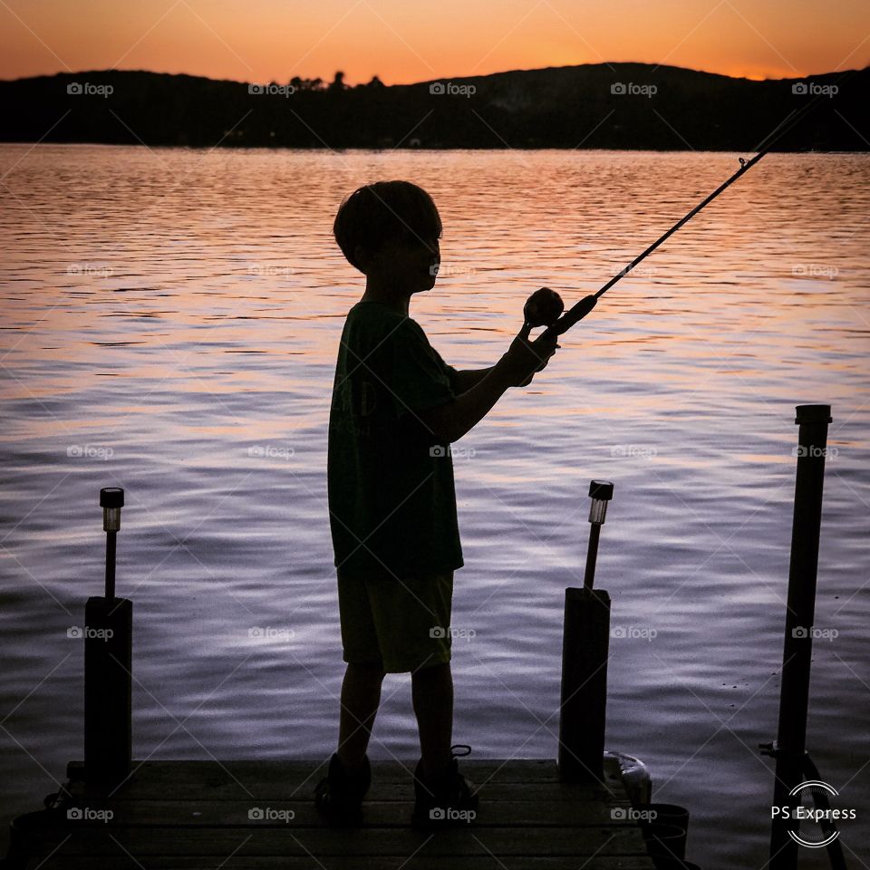 Boy silhouette fishing in lake leisurely beautiful sunset