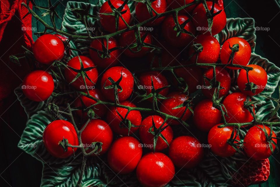 The vibrant red color of flamenco and cherry tomatoes is incredibly delicious, and they are presented on a green background with drops of water.