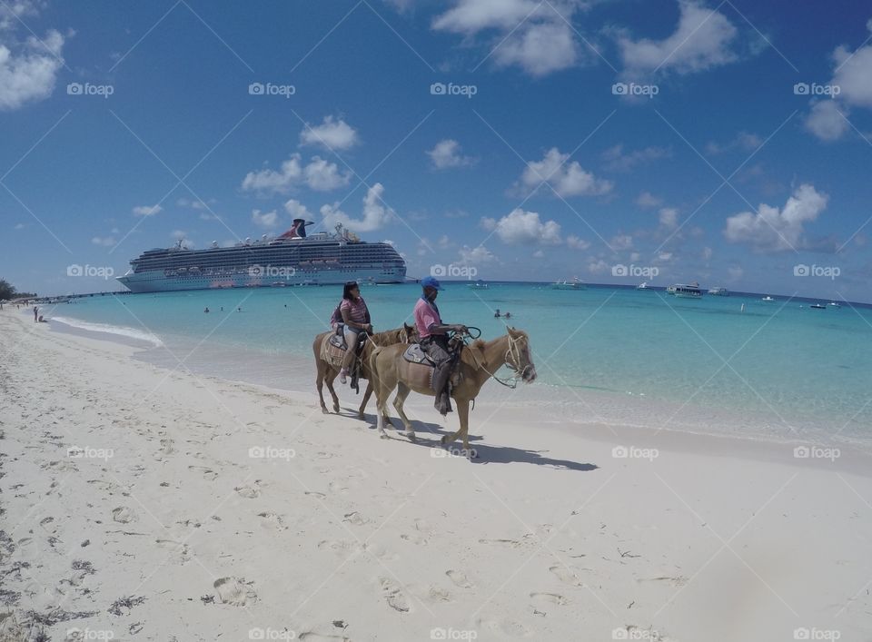 People on horseback on walking on a beach vacation tourism with cruise ship in the background and ocean