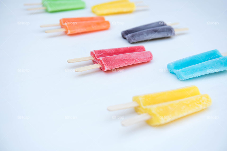 Isolated image of a row of brightly colored popsicles arranged in a pattern on a white background