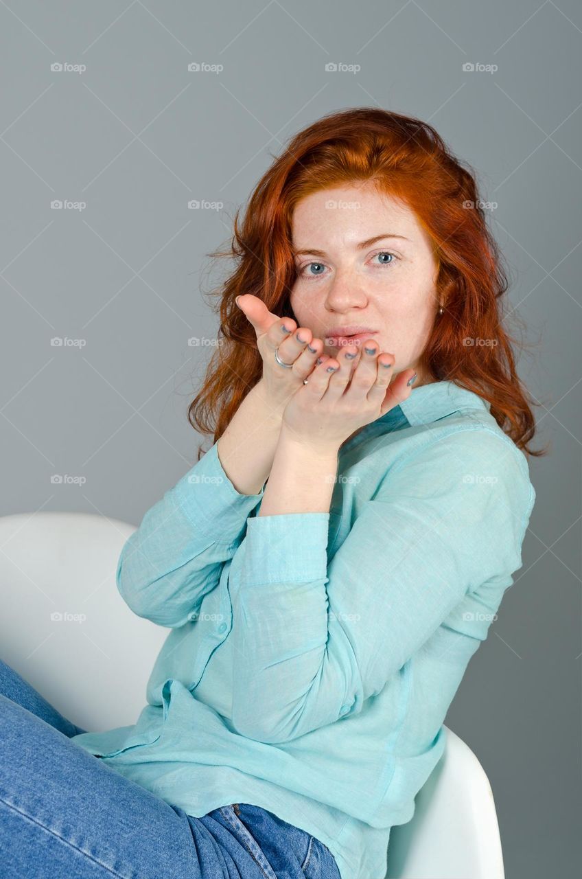 Lifestyle portrait of beautiful,  cute, attractive redhead woman with freckles,  blue eyes,  curly hair sitting in the arm chair.  Natural beauty