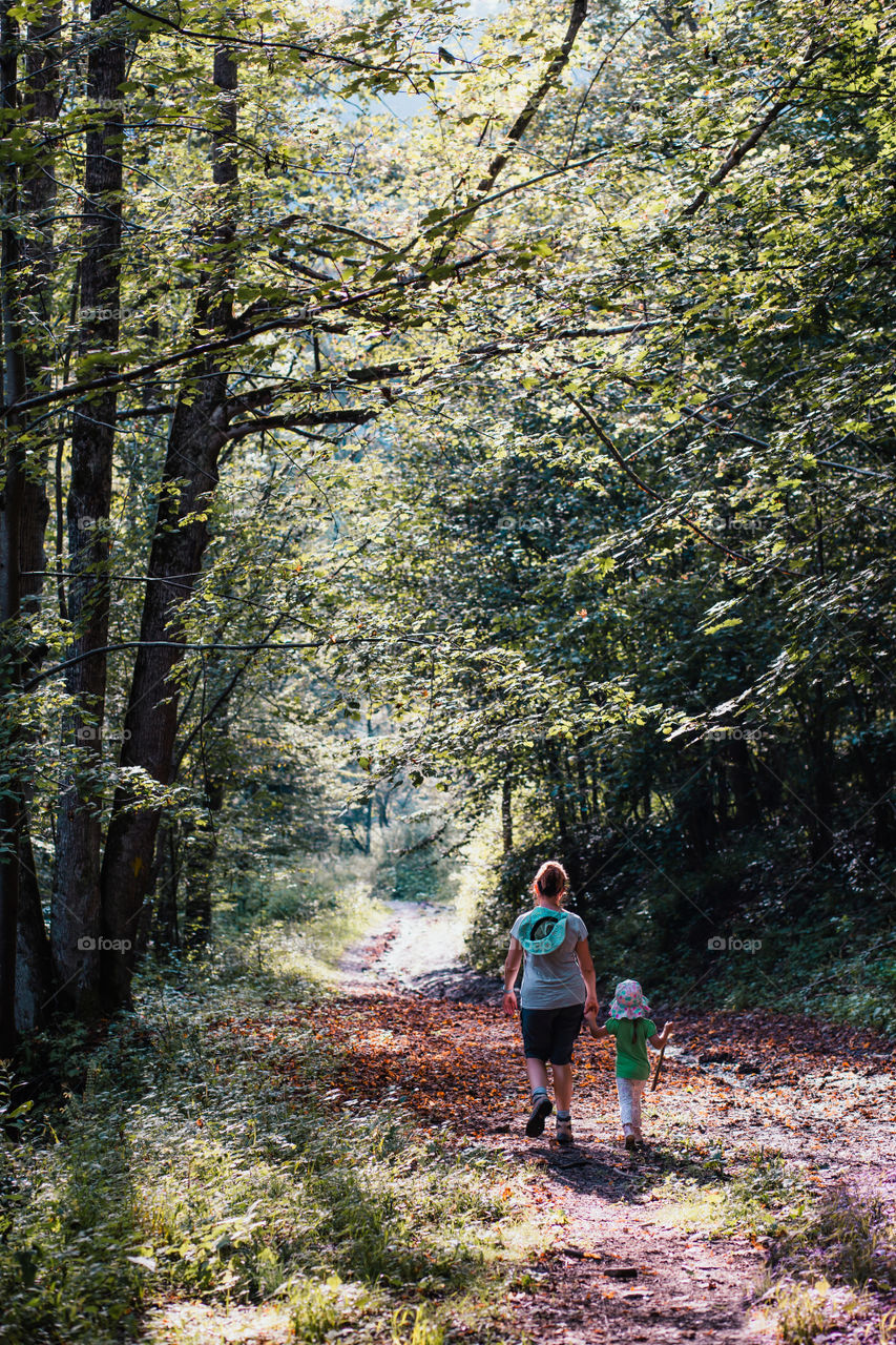 Mother with daughter walking through the forest. Spending vacation on wandering in forests