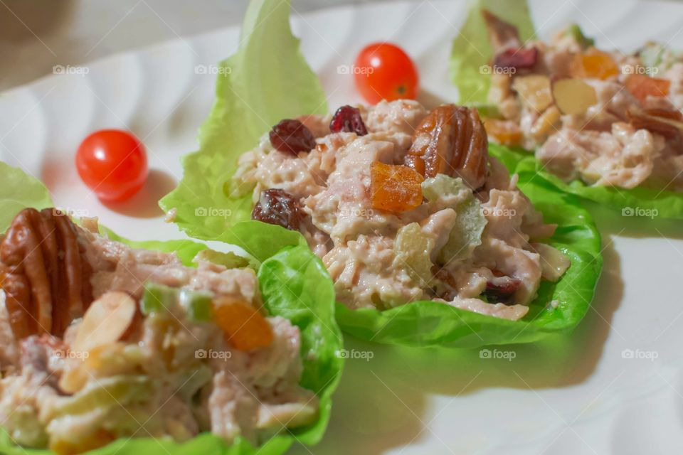 gourmet rotisserie chicken salad in green lettuce wraps served on a white plate with cherry tomatoes