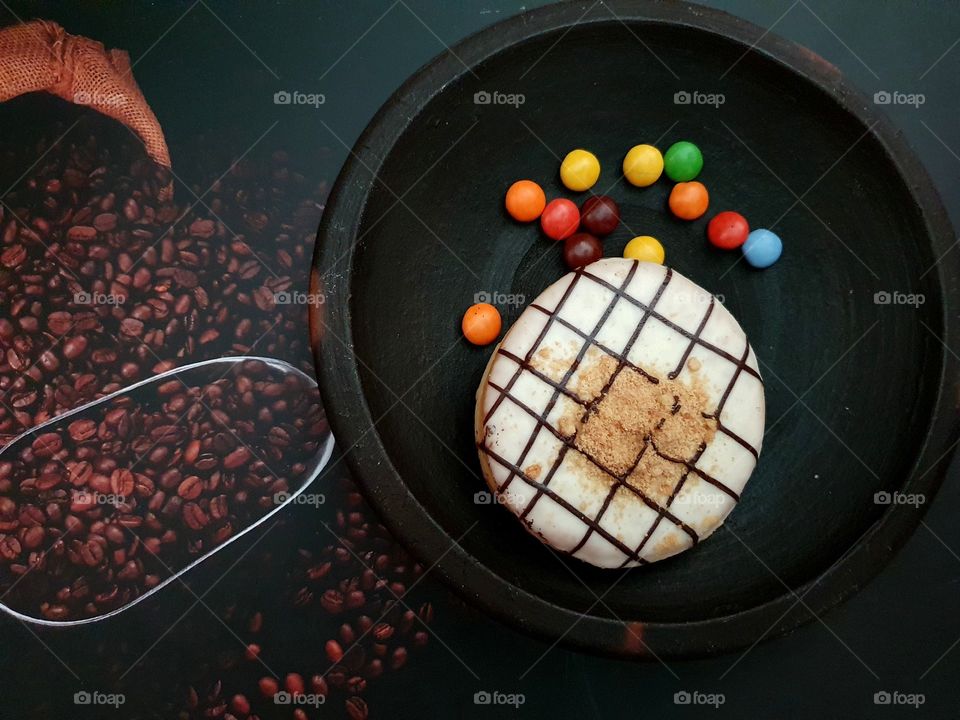Donuts decorated with white chocolate and sprinkled with nuts,placed on a clay plate.Beside the donuts put some chocolate chips