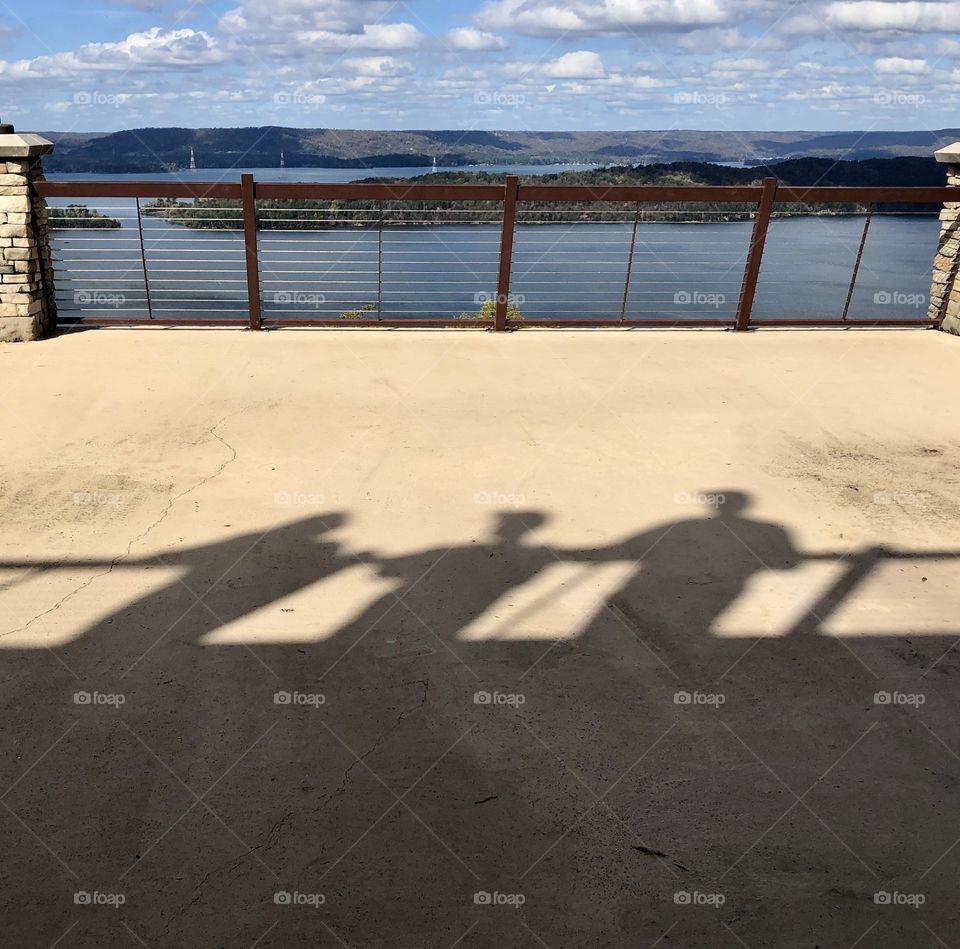 Shadows of three people on balcony overlooking lake and hills