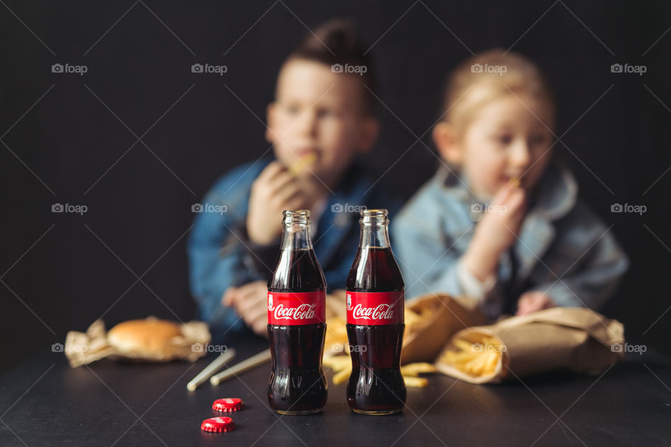 stylish children, dressed in denim clothes, drinking Coca-Cola.  They eat, relax, communicate at home.  sister and brother drink coca cola