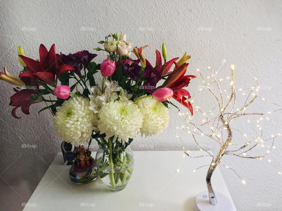 Red white and pink flowers in a vase standing on a white chest of drawers.