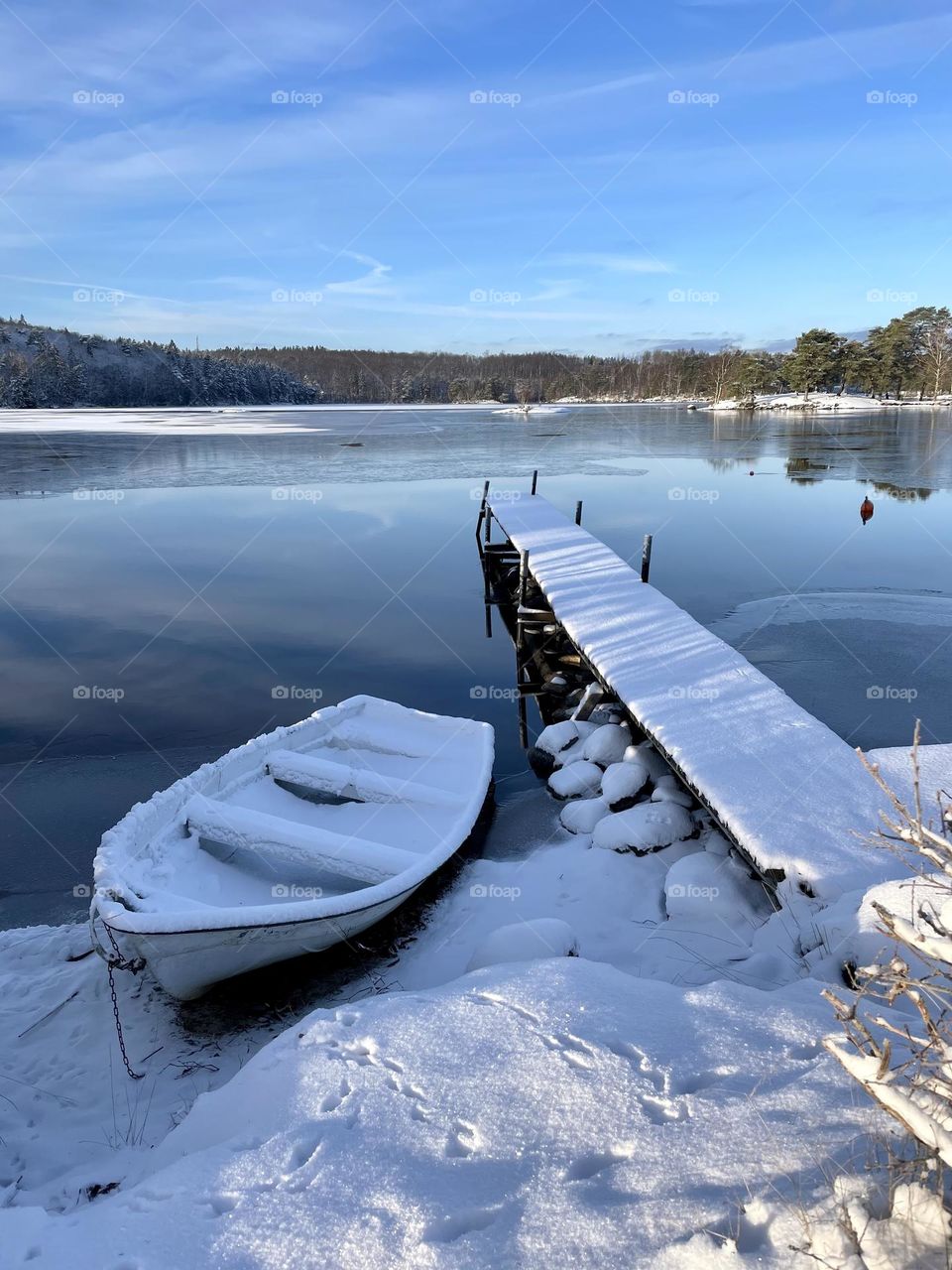 Beautiful winter day by peaceful lake, boat and wooden pier covered with snow and ice 
