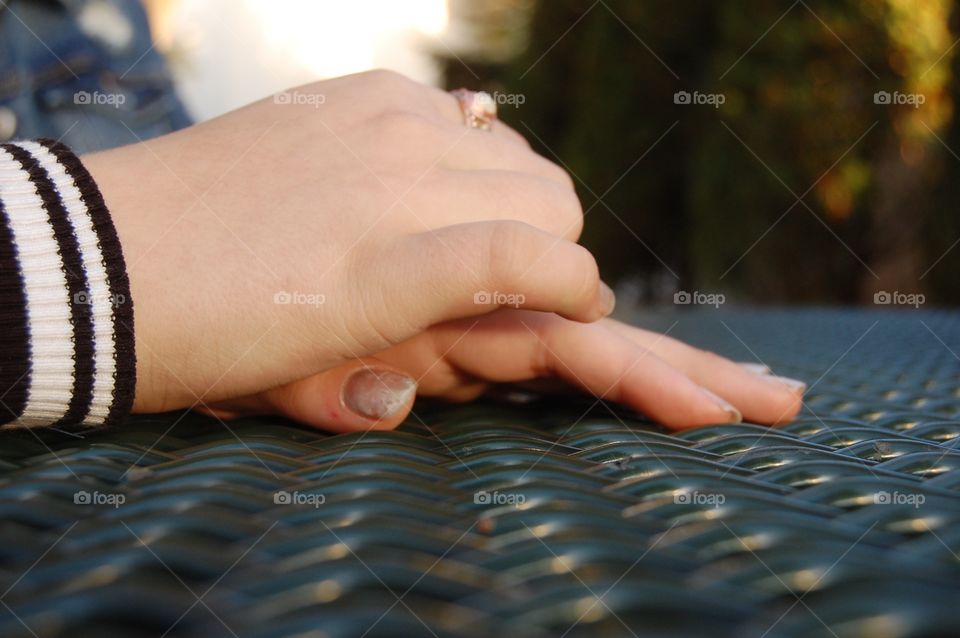 A picture of a girls hands on a picnic table. She is wearing an interesting ring.