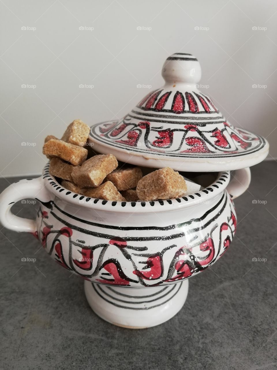 Multicoloured and patterned sugar container with handles and striped top and leg is full of white and brown sugar