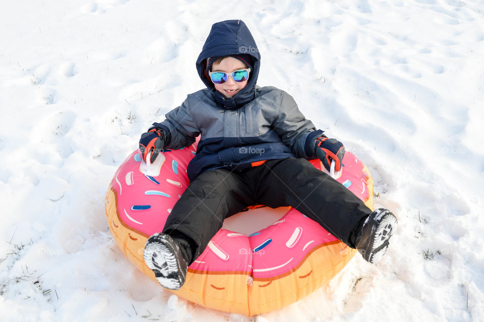 Young boy sitting in a donut innertube in the snow during winter