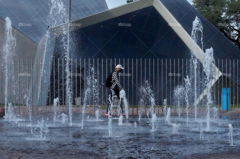 Man walking in front of a water fountain. Photo of cold tones.