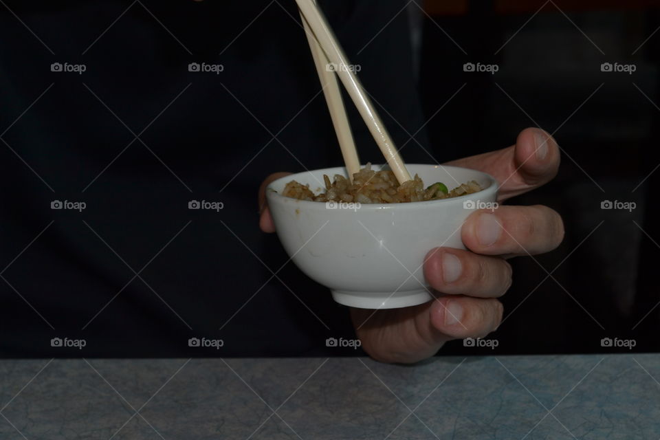 Closeup bowl of Chinese fried rice food in small bowl, person's hand eating with chopsticks