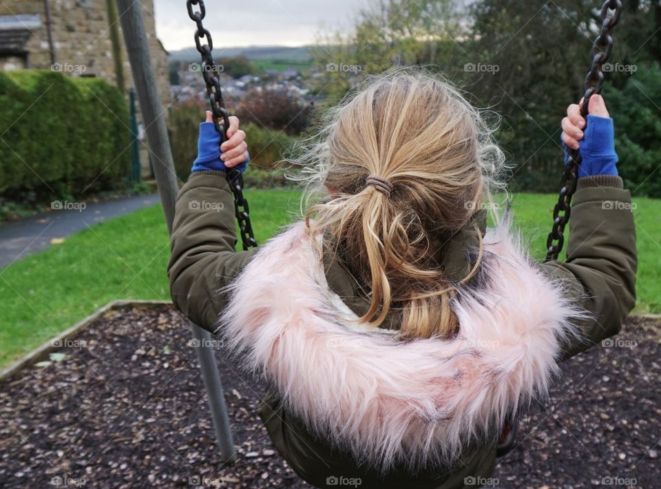 Playing on a swing with views of Settle .. girl with pink fur hood.
