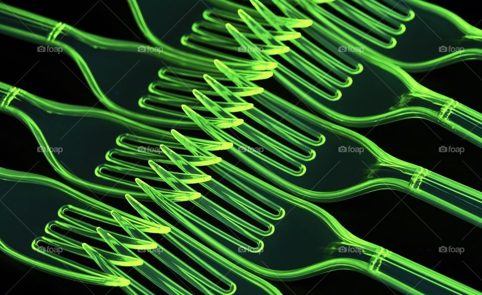 Black light abstract of fluorescent green plastic forks 