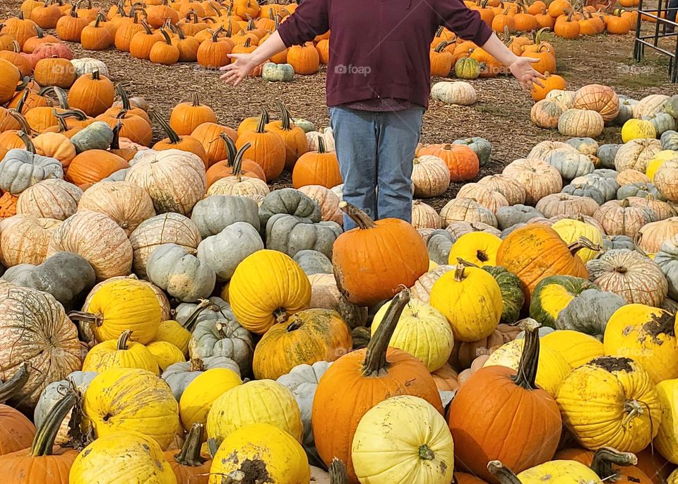 woman wearing jeans and a sweatshirt standing in a pumpkin patch at an Oregon farm in Autumn