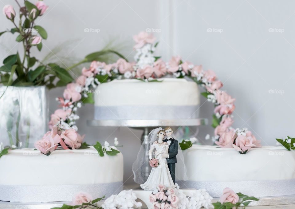 A wedding cake with pink icing flowers and bride & groom figurines.