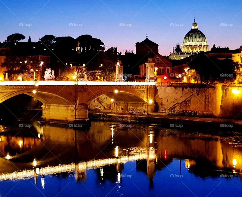 View across the Tiber River towards the illuminated dome of St Peter's Basilica, taken at dusk in Rome.