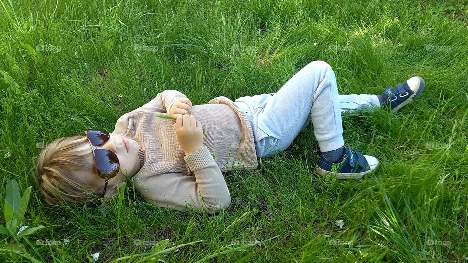 little boy wearing sunglasses is lying on the grass