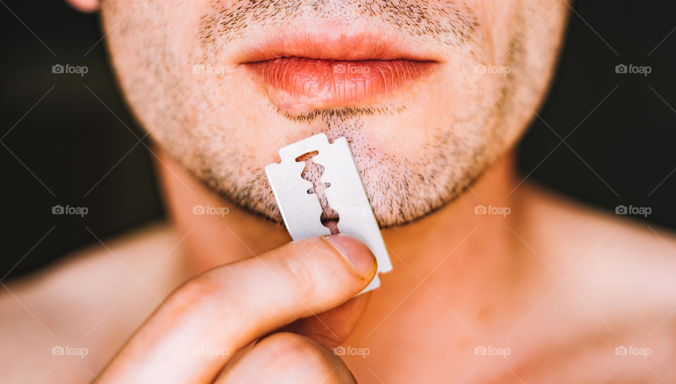 Man holding razor blade against chin