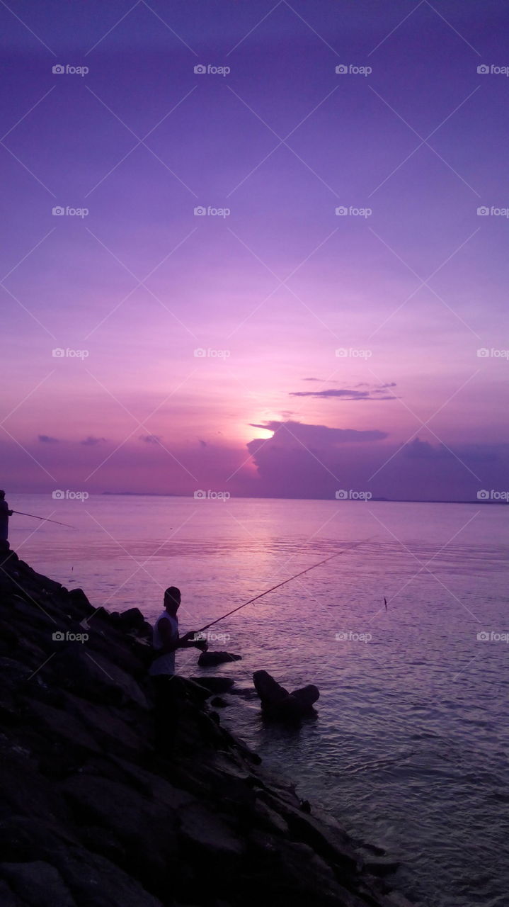 a violet sunset by the beach, when ther're a fisherman waiting for his fish 🐟 and this was taken through a sunglasses.