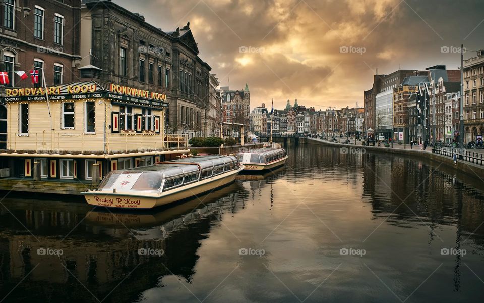 Beautiful architecture and boats in the canal under dramatic cloudy skies at Amsterdam, Netherlands