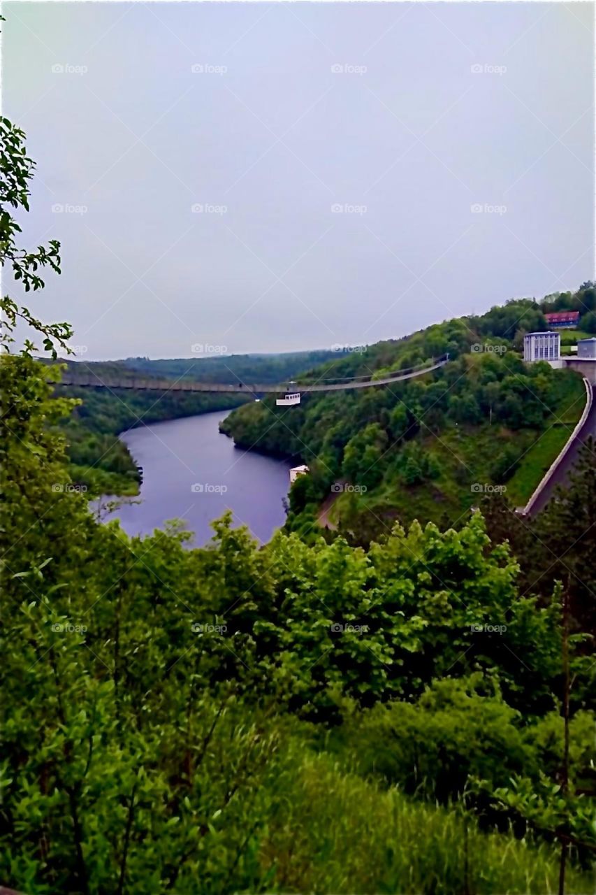 This is the „Rappbode Dam“ with water reservoir and power plant by „Oberharz“, “Harz“, „Saxony-Anhalt“ in former „East Germany“, the „DDR“ or „German Democratic Republic“. A long hanging bridge leads across the reservoir. 2024. Hypnotic Productions