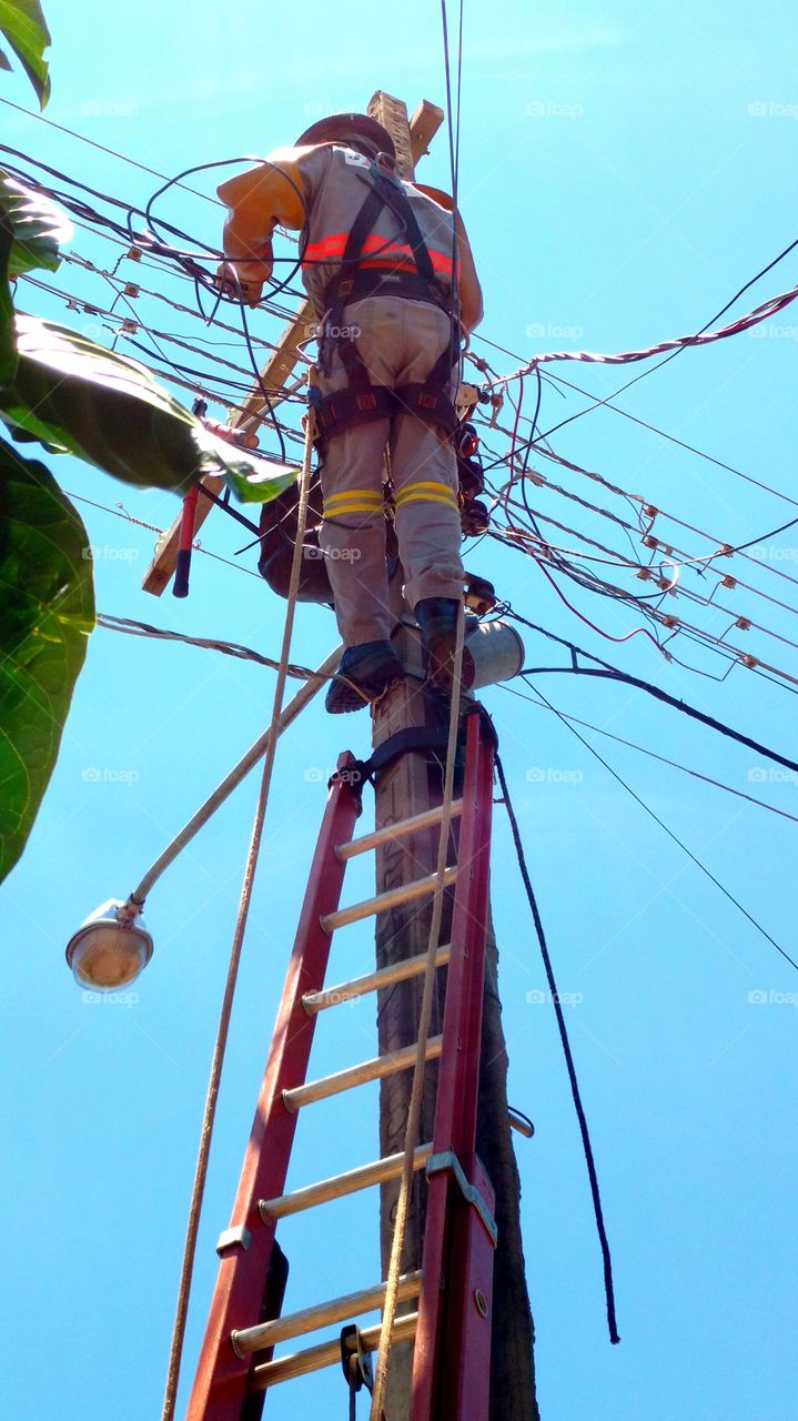 Homem ao poste, na escada. Energia, eletricidade, rede elétrica da rua.