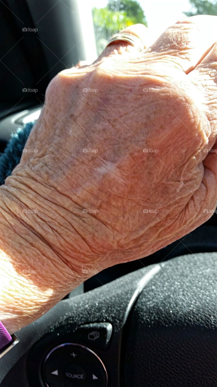 Aging hand on a steering wheel.