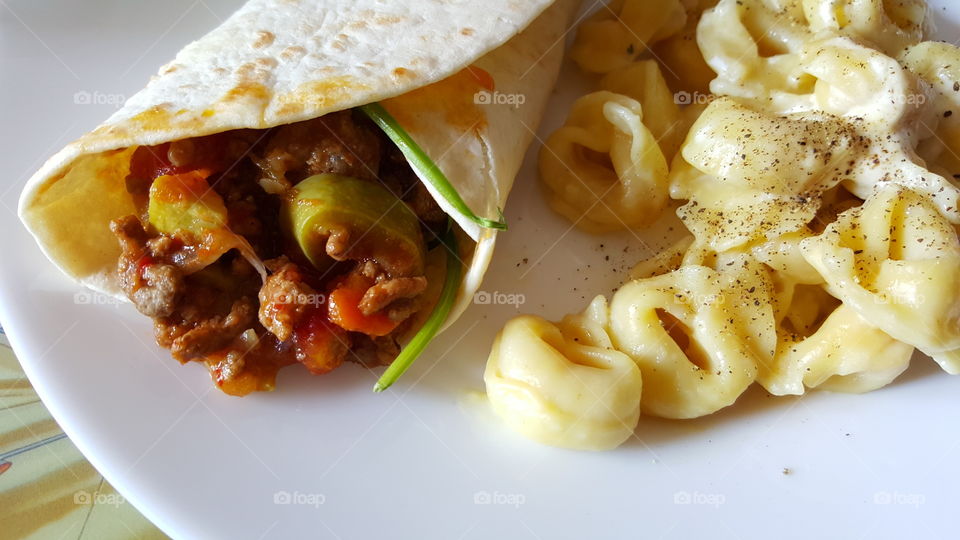 Beef and Bean Burritos. with spicy chili bean sauce,  squash,  cheddar cheese and tortellini pasta served on a plate.