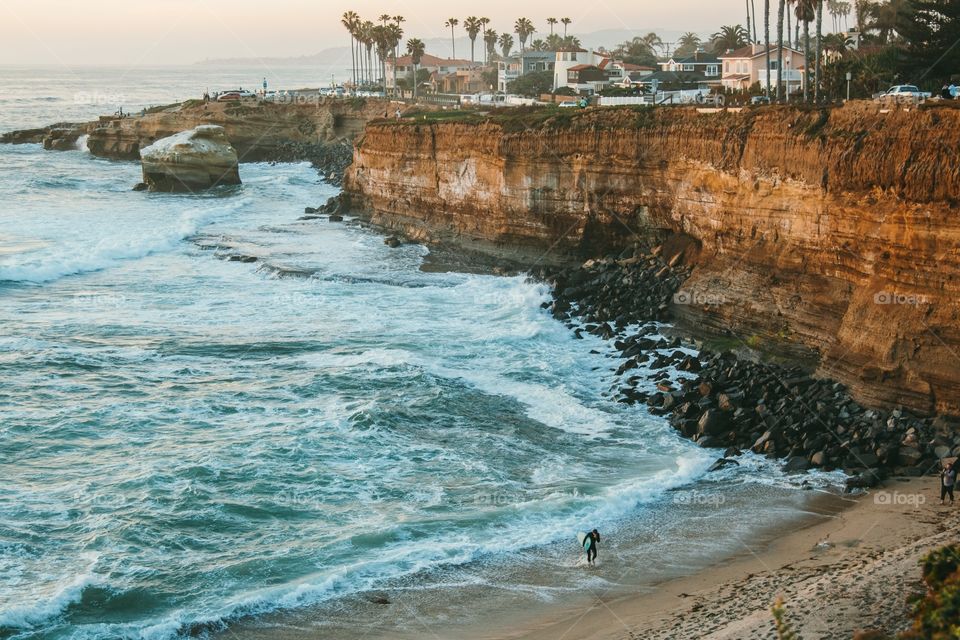 A surfer leaves the lineup as light fades over the iconic Sunset Cliffs of San Diego