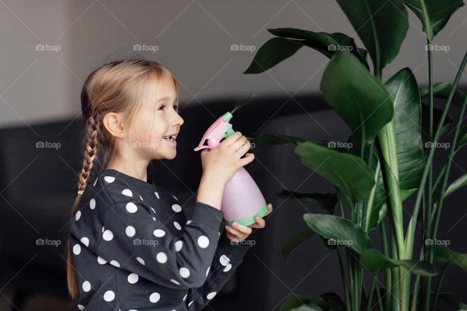 Little Caucasian girl spraying plant at home 