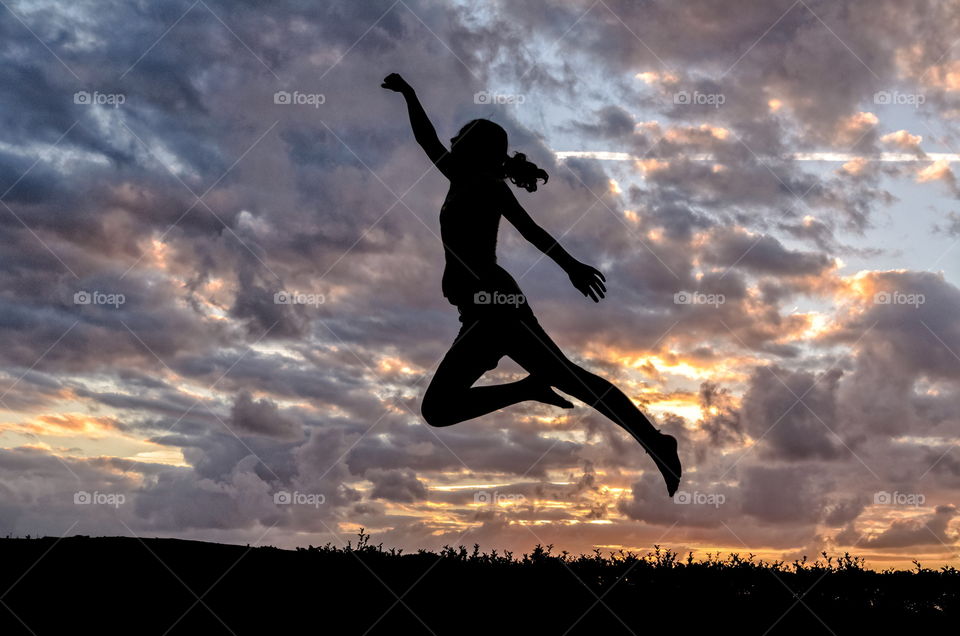 Silhouette of a girl jumping as a super heroe at sunset
