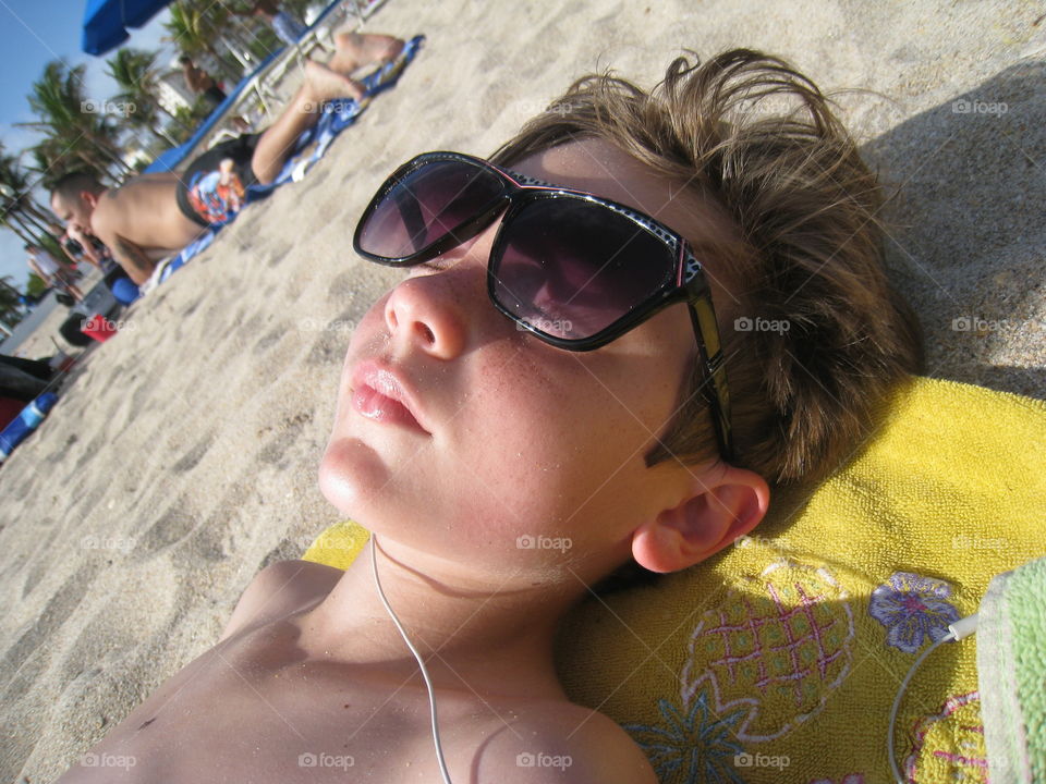 Tan me. Young boy tanning and listening to music at the beach 