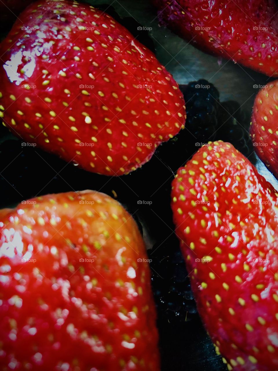 Beautiful, bright red and fresh strawberries with blackberries sitting at the bottom of the bowl filled with water. 