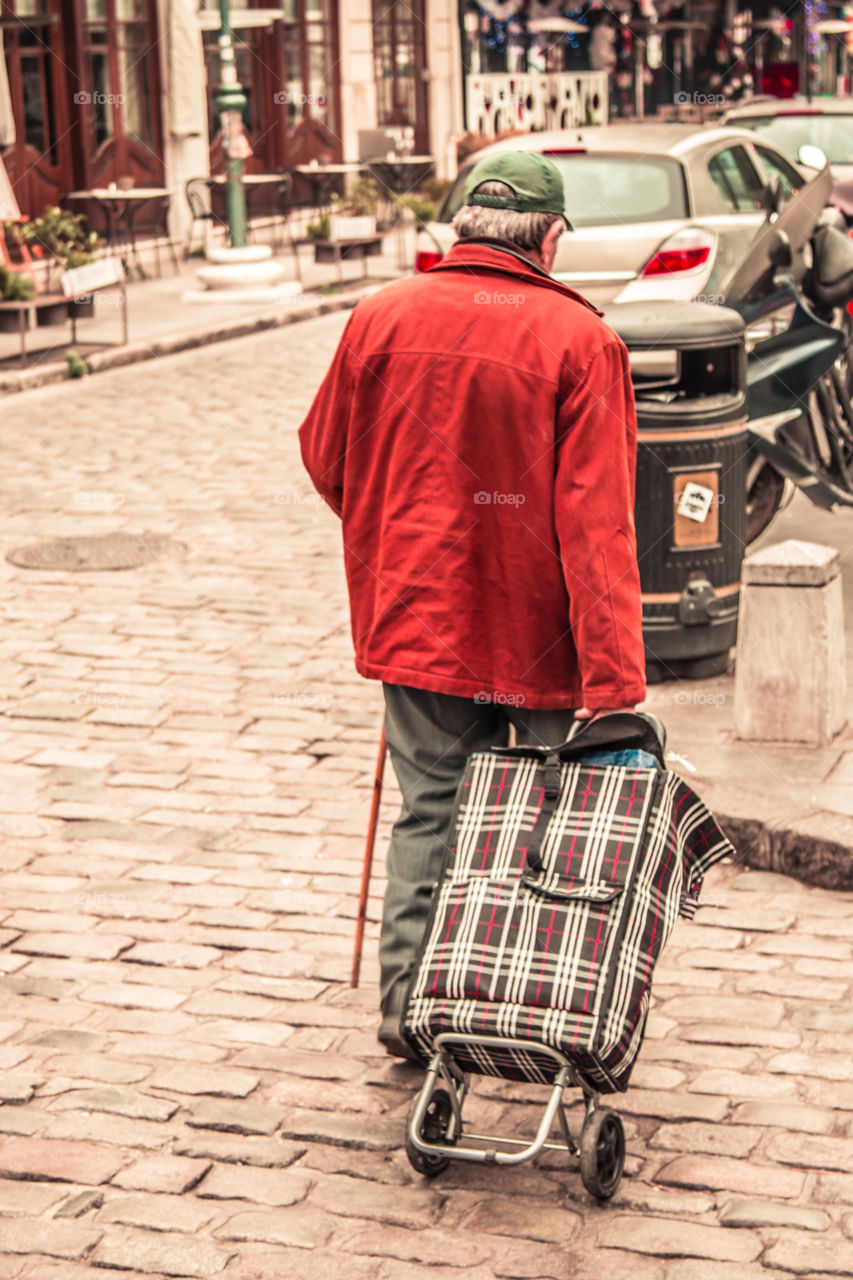 Elderly Man With Walking Stick And Shopping Cart In The Street
